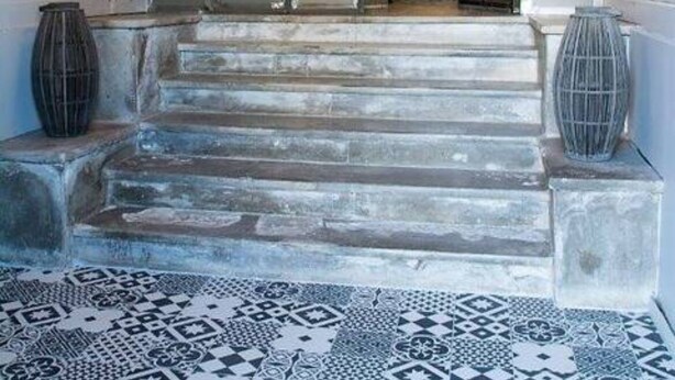 Eine imposante Treppe führt zu einer zweiten Etage mit einem gemusterten Boden und je einer großen Vase auf jeder Seite.