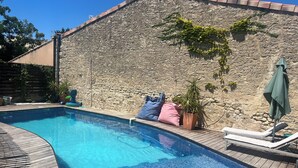 Ein Schwimmbecken mit Steinmauer, Liegestühlen und einer Topfpflanze.