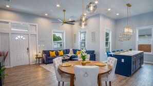 Ein modernes Wohnzimmer mit Sofa, Esstisch, Stühlen, Deckenventilator und einer Küche mit blauer Kochinsel.