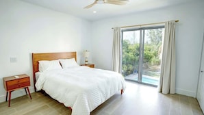 A bedroom with a large bed, wooden headboard, a nightstand, a ceiling fan, and a view of a swimming pool through a sliding glass door. - NEW LuxuryCondo Location Pool, BahaMar UNIT 5 (Nassau)