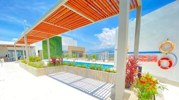 A modern outdoor pool area with a wooden pergola, a landscaped garden, and a view of the surrounding landscape.