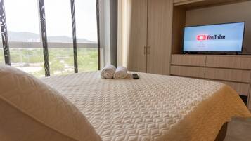A hotel room with a bed, a TV displaying the YouTube logo, and a view of the outdoors.