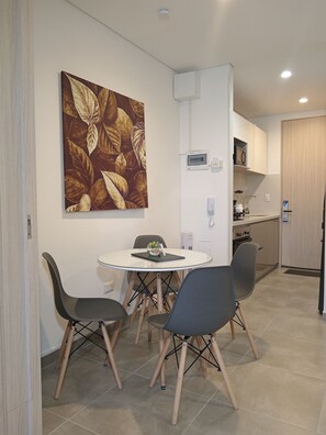 A dining area with a round table, four chairs, a wall-mounted painting, a kitchen in the background, and a door leading to another room. - salguero suite 313 (Santa Marta)