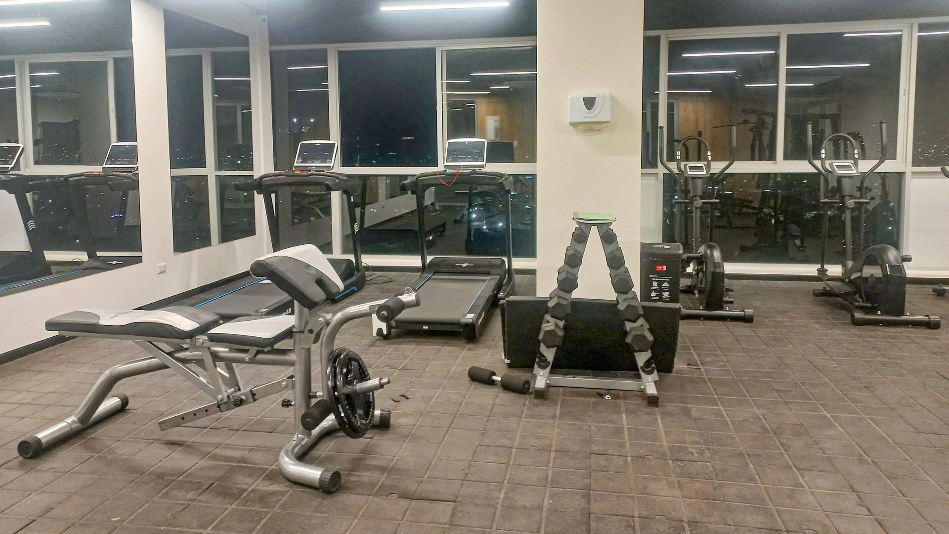 A gym with exercise equipment, large windows, and a tiled floor.