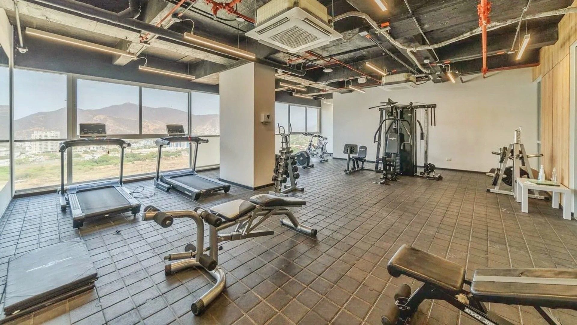 A gym with treadmills, weight machines, and a view of mountains through large windows.