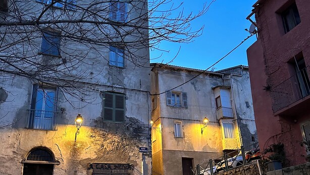 A cobblestone street with buildings featuring arched doorways and a staircase leading to a higher level.