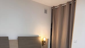 A neatly made bed with white linens, a headboard with a light fixture, and a bedside table with a remote control.