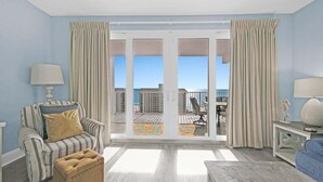 A living room with a striped armchair, ottoman, and a view of the balcony with outdoor furniture. - Laketown Wharf 1120 (Panama City Beach)