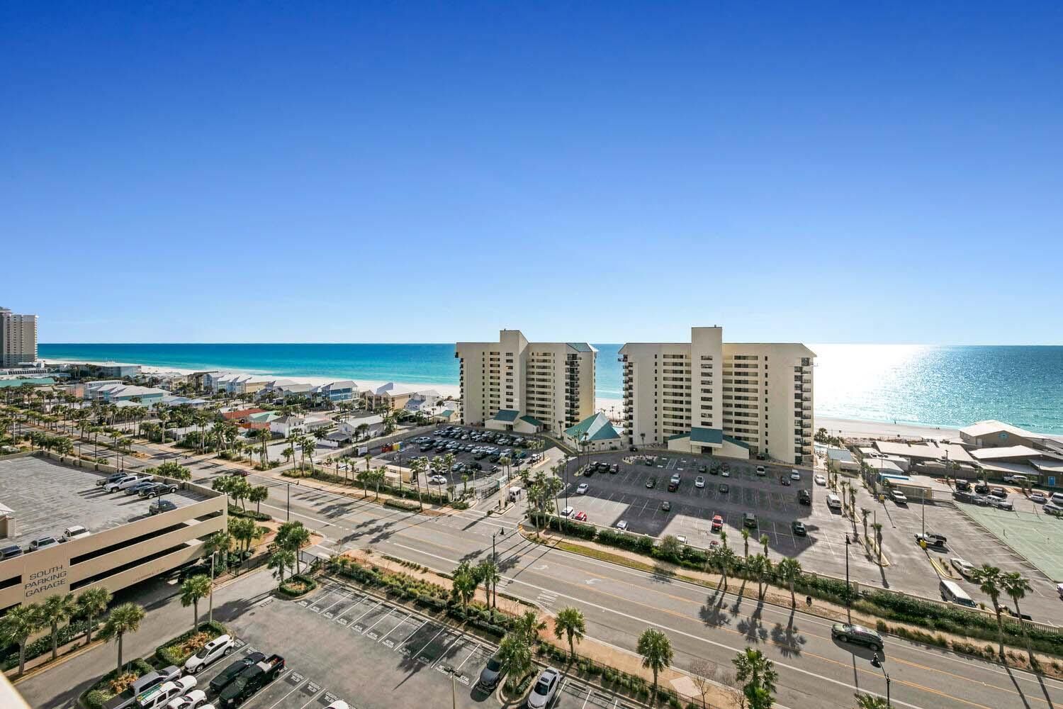 A coastal hotel with multiple high-rise buildings, a parking lot, and a view of the beach.