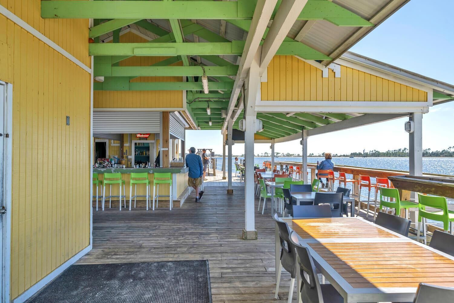 An outdoor bar area with wooden tables and chairs, a bar counter, and a view of the water.