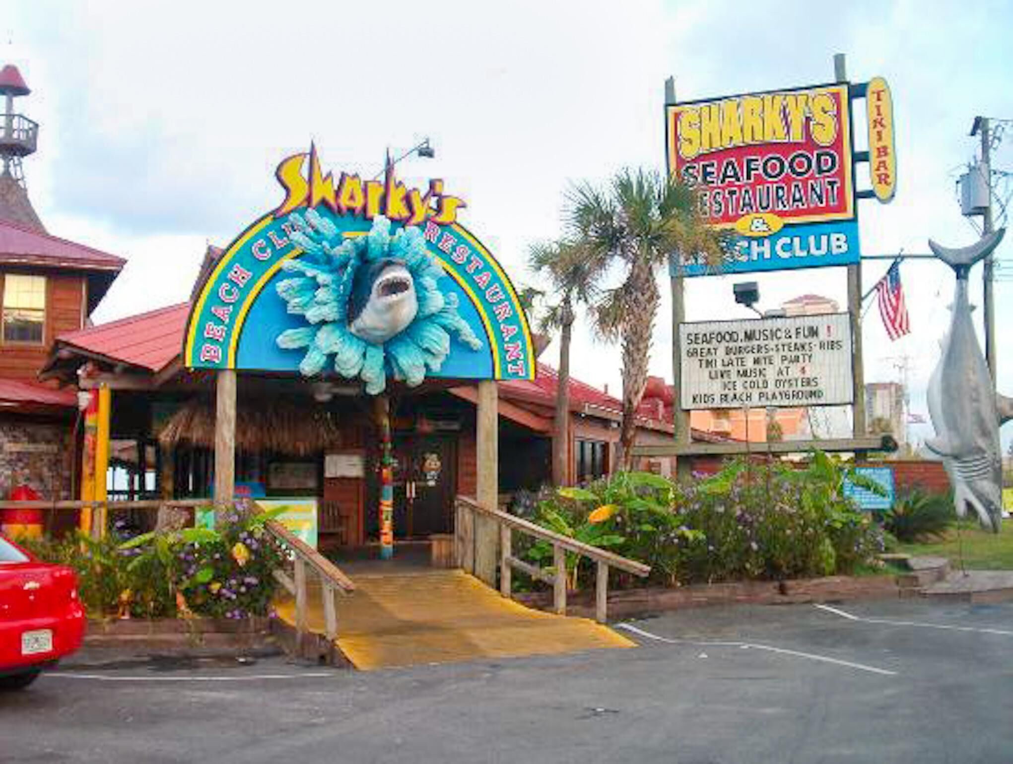 Un restaurante frente a la playa llamado Sharky's Seafood Restaurant, con un letrero de un tiburón como mascota.