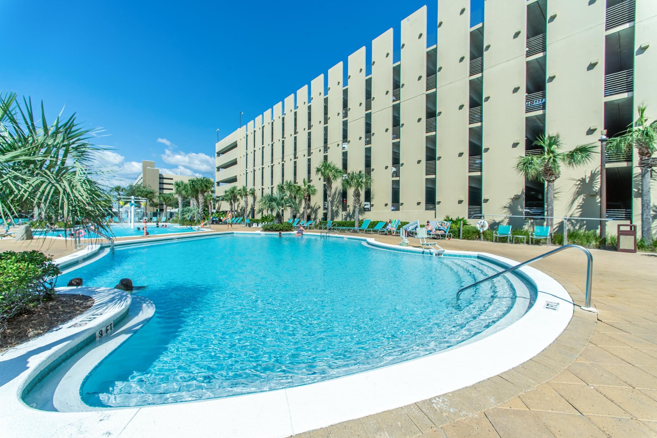 A swimming pool with a curved edge, surrounded by lounge chairs and palm trees.