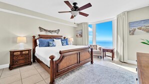 Une chambre spacieuse avec un grand lit, un ventilateur de plafond, une vue sur l’océan et un coin salon confortable.