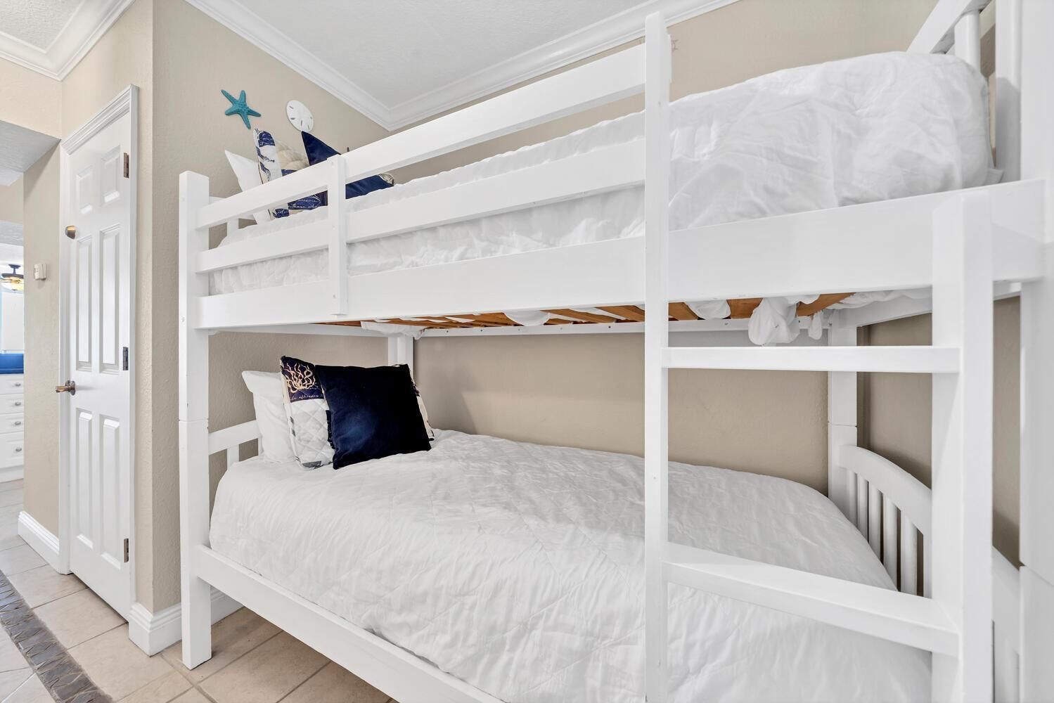 A bunk bed with white bedding and a dark blue pillow.