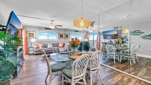 A spacious living area with a dining table, chairs, and a large mirror reflecting the room.