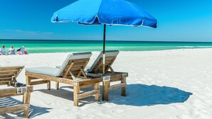A beach scene with wooden lounge chairs and a blue umbrella.