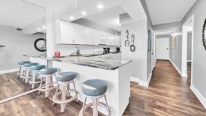 A modern kitchen with white cabinets, a marble countertop, and bar stools.