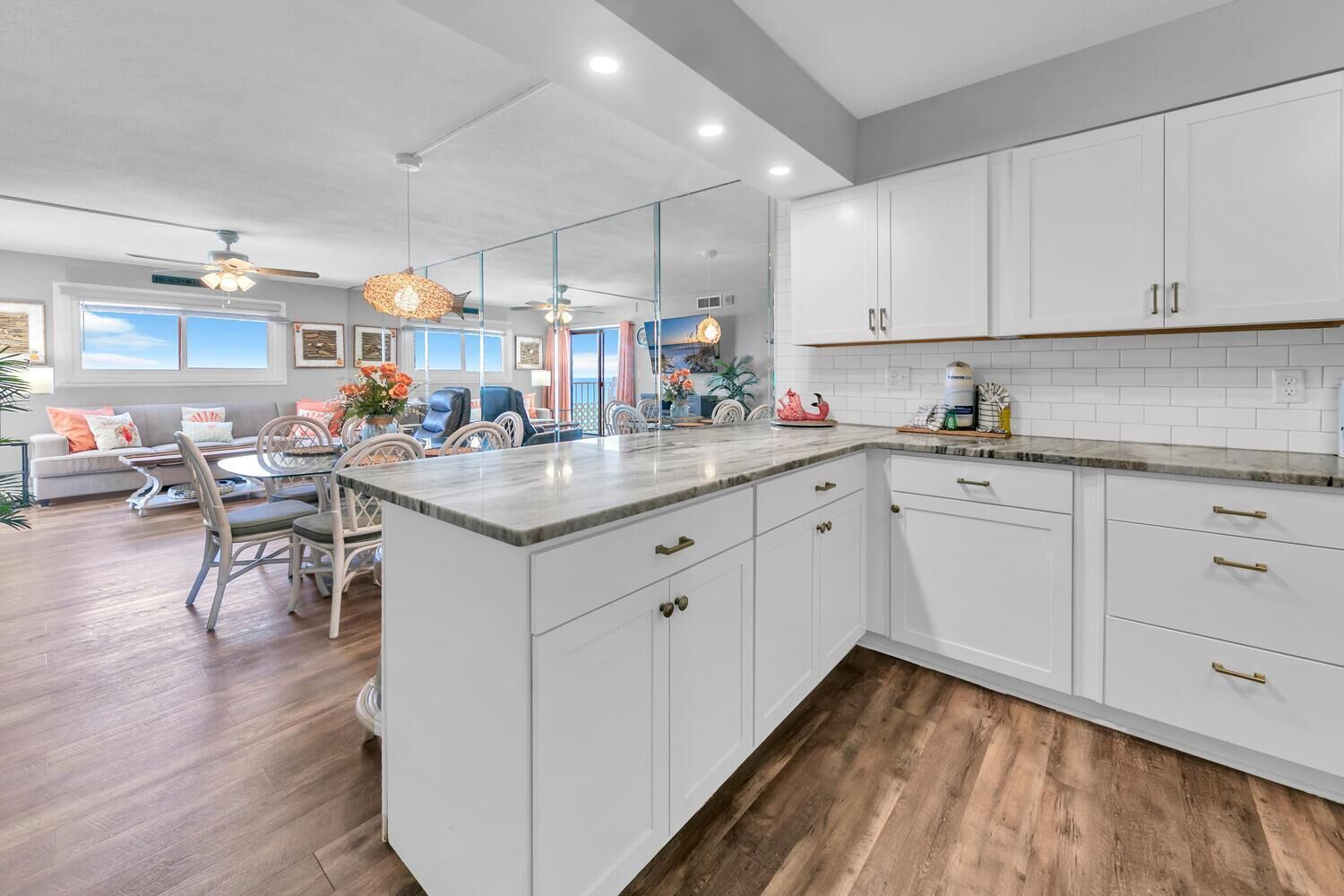 A modern kitchen with white cabinets, a marble countertop, and wooden flooring.