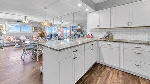 A modern kitchen with white cabinets, a marble countertop, and wooden flooring.