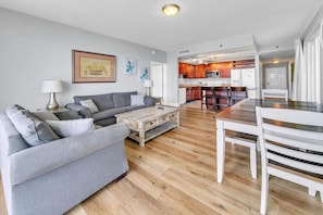 A modern living room with a grey sofa set, a wooden coffee table, and a dining area with a white table and chairs. - Laketown Wharf 801 (Panama City Beach)