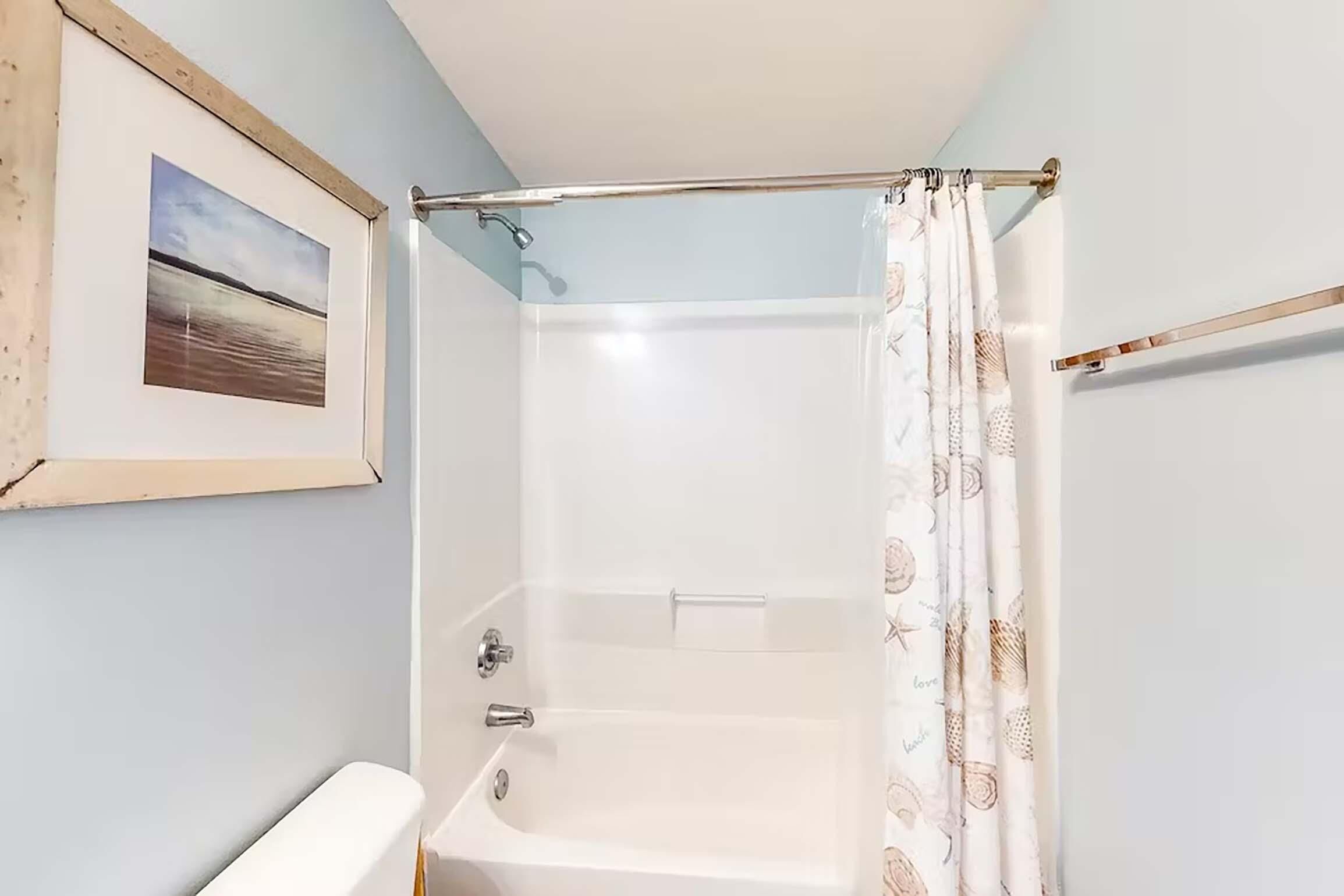 Ein Badezimmer mit einer Badewanne, einer Duschvorhang und einem gerahmten Bild an der Wand.