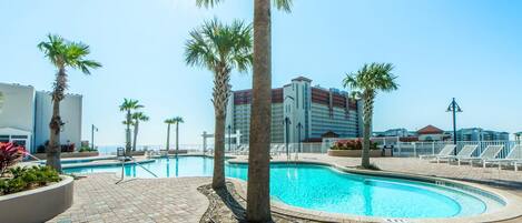 A swimming pool with palm trees, lounge chairs, and a clear blue sky.