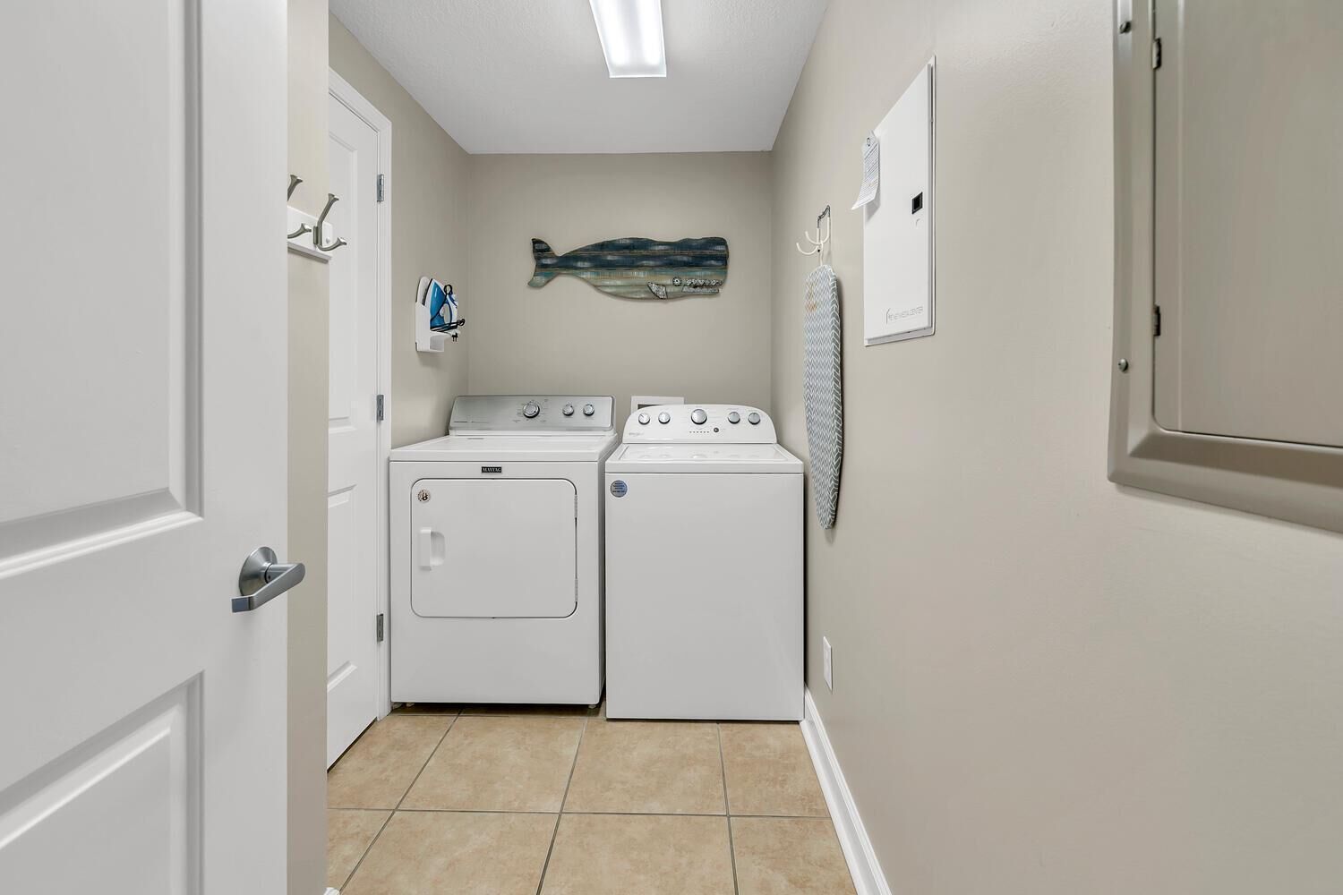 A laundry room with two white washers and dryers, a fish-shaped wall decoration, and a tiled floor.