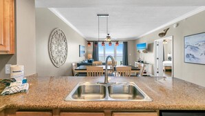 A modern kitchen with granite countertops, stainless steel sink, wooden cabinets, and a dishwasher. - Marisol 204 (Panama City Beach)