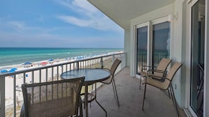 A balcony with a view of the beach, wicker chairs, a table, and a glass door. - Marisol 204 (Panama City Beach)