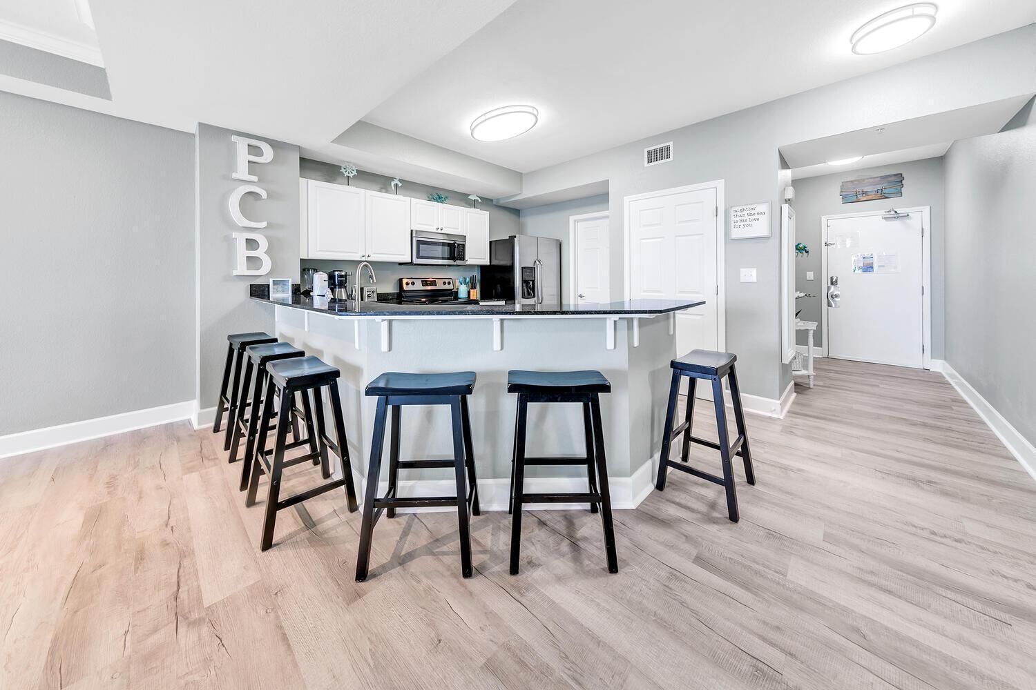 A modern kitchen with white cabinets, a central island with stools, and a microwave.