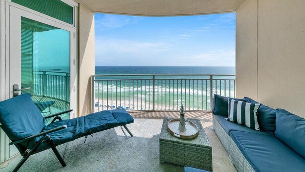 Un balcone con vista sulla spiaggia, una sedia a sdraio, un divano e un tavolino con una candela.