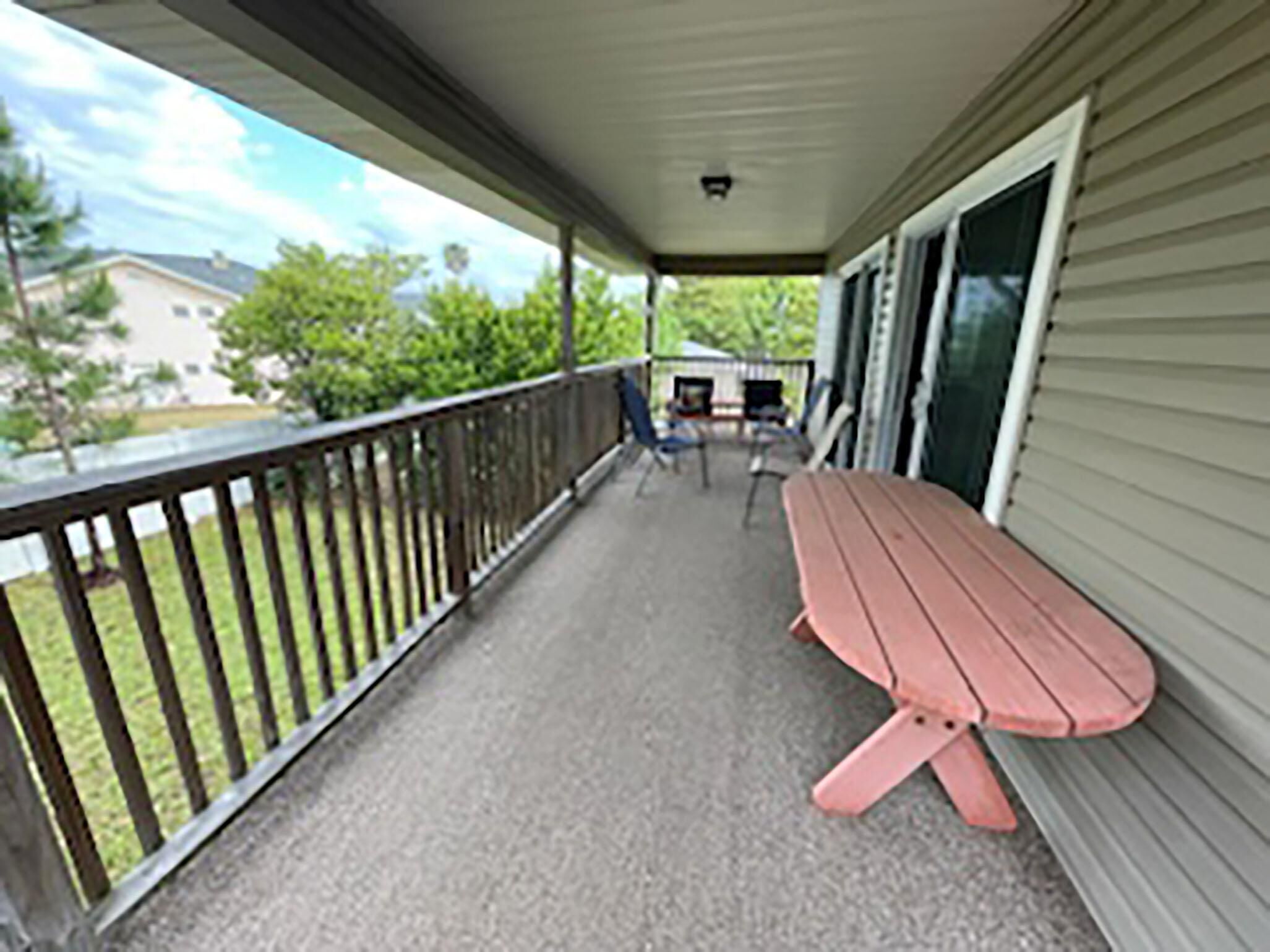 A covered porch with a picnic table and chairs, a railing, and a view of a house and trees.