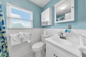 A bathroom with a toilet, sink, and mirror. There are towels hanging on a rack and a window with blinds. - Beach Haven (Panama City Beach)