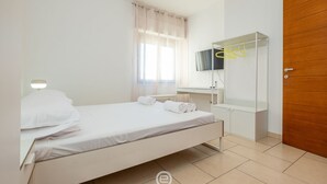 Ein Schlafzimmer mit einem Bett, einem Schreibtisch, einem Fernseher und einer Holztür.