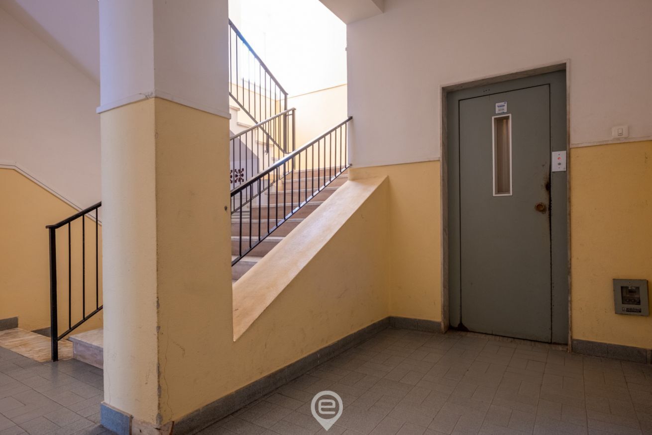 Una escalera que conduce a un piso superior, una puerta con un pequeño ventanal y un suelo de baldosas.