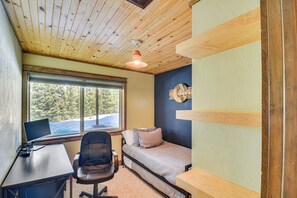 Una habitación con techo de madera, un escritorio con ordenador, una cama y una ventana con vistas a árboles.