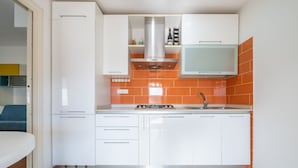 A compact kitchen with white cabinets, an orange backsplash, a stainless steel range hood, and a built-in microwave.