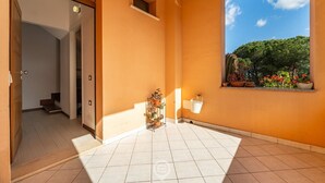 A spacious room with a tiled floor, a window with a view of greenery, and a small plant stand.