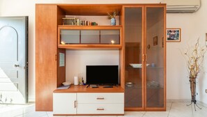 A room with a wooden entertainment unit, a television, and a glass cabinet. - Dahlia Apartment (Cabras)