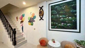 A staircase with a black balustrade, a wall with a large framed painting of water lilies, and two chairs with cushions. - Ians Home (Dongshan)