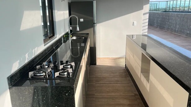 A modern kitchen with a black granite countertop, stainless steel appliances, and a wooden floor. - Flat 304 Porto Prime com Rooftop e Piscina (Porto de Galinhas Ipojuca)