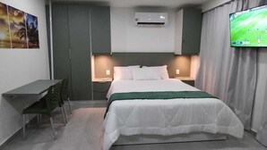 A hotel room with a bed, bedside tables, a desk, and a TV mounted on the wall. - Flat 304 Porto Prime com Rooftop e Piscina (Porto de Galinhas Ipojuca)