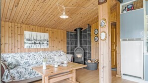 Ein gemütliches Blockhaussinnere mit Holzbalkendecke, einer Couch, einem Tisch, einem Kamin und einem Kühlschrank.