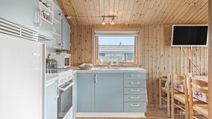 Eine kompakte Küche mit integriertem Backofen, Mikrowelle und Spüle. Ein Holztisch mit Stühlen und ein an der Wand befestigter Fernseher sind vorhanden.