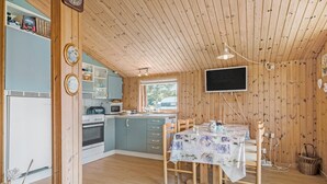 Eine gemütliche Küche mit Holzwänden, einem Esstisch mit Blumenmuster-Tischdecke und einem an der Wand befestigten Fernseher.