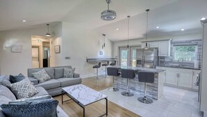 Ein modernes Wohnzimmer mit einem grauen Sofa, einem Couchtisch und einer Küchenzeile mit Bar und weißen Schränken.