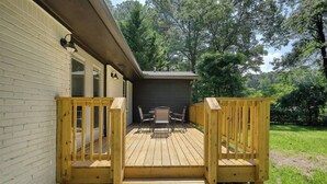 Eine Holzterrasse mit Tisch und Stühlen, einem überdachten Bereich und einem umzäunten Garten.
