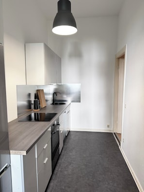 A modern kitchen with a dark countertop, stainless steel appliances, and a pendant light.