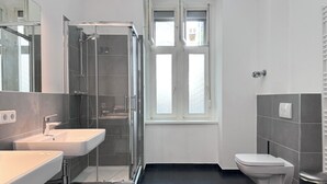 Ett modernt badrum med en dusch som är avskärmad med glasväggar, ett handfat och en toalett.