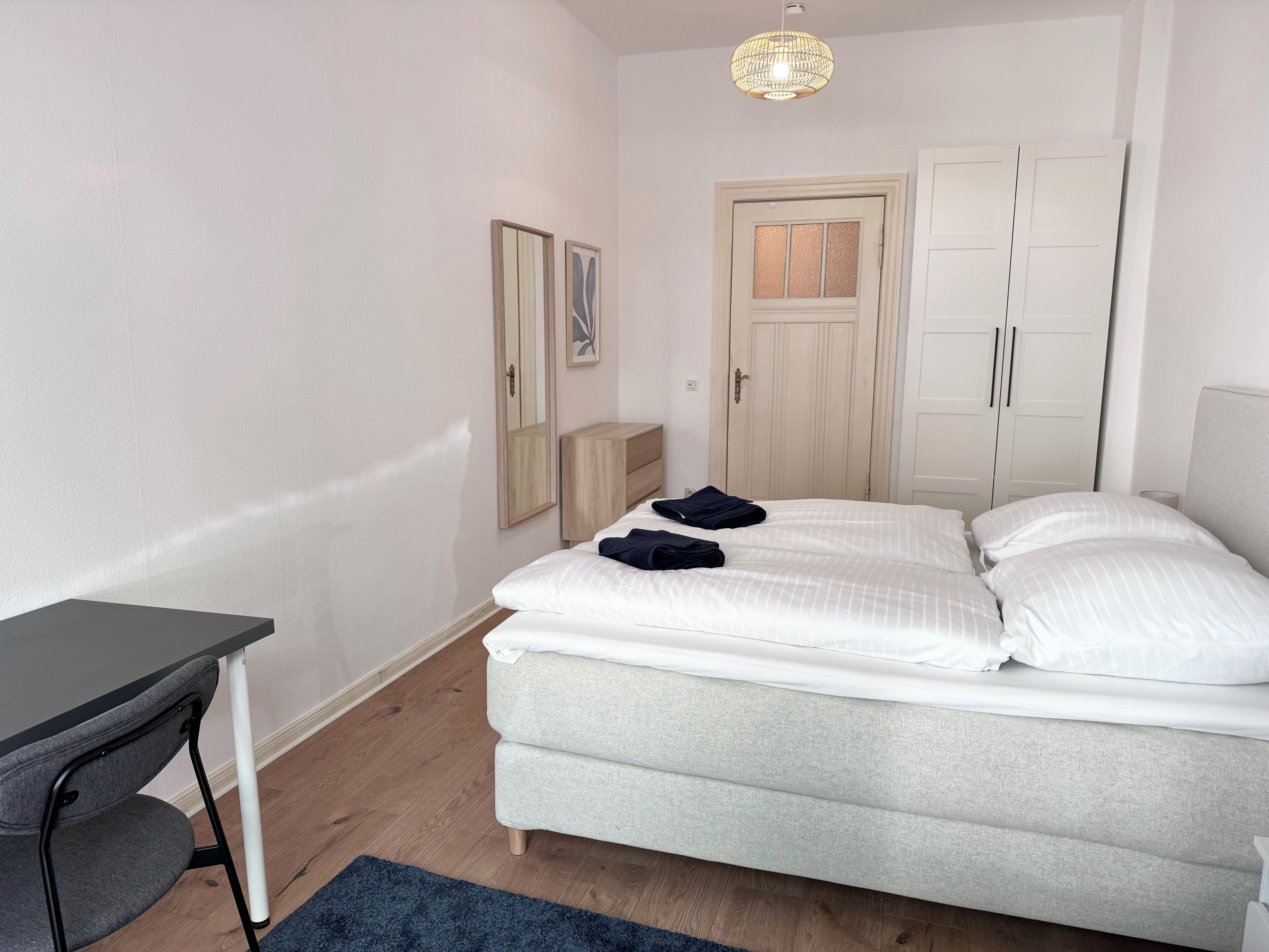 A neatly arranged bedroom with a bed, a desk, and a wardrobe.